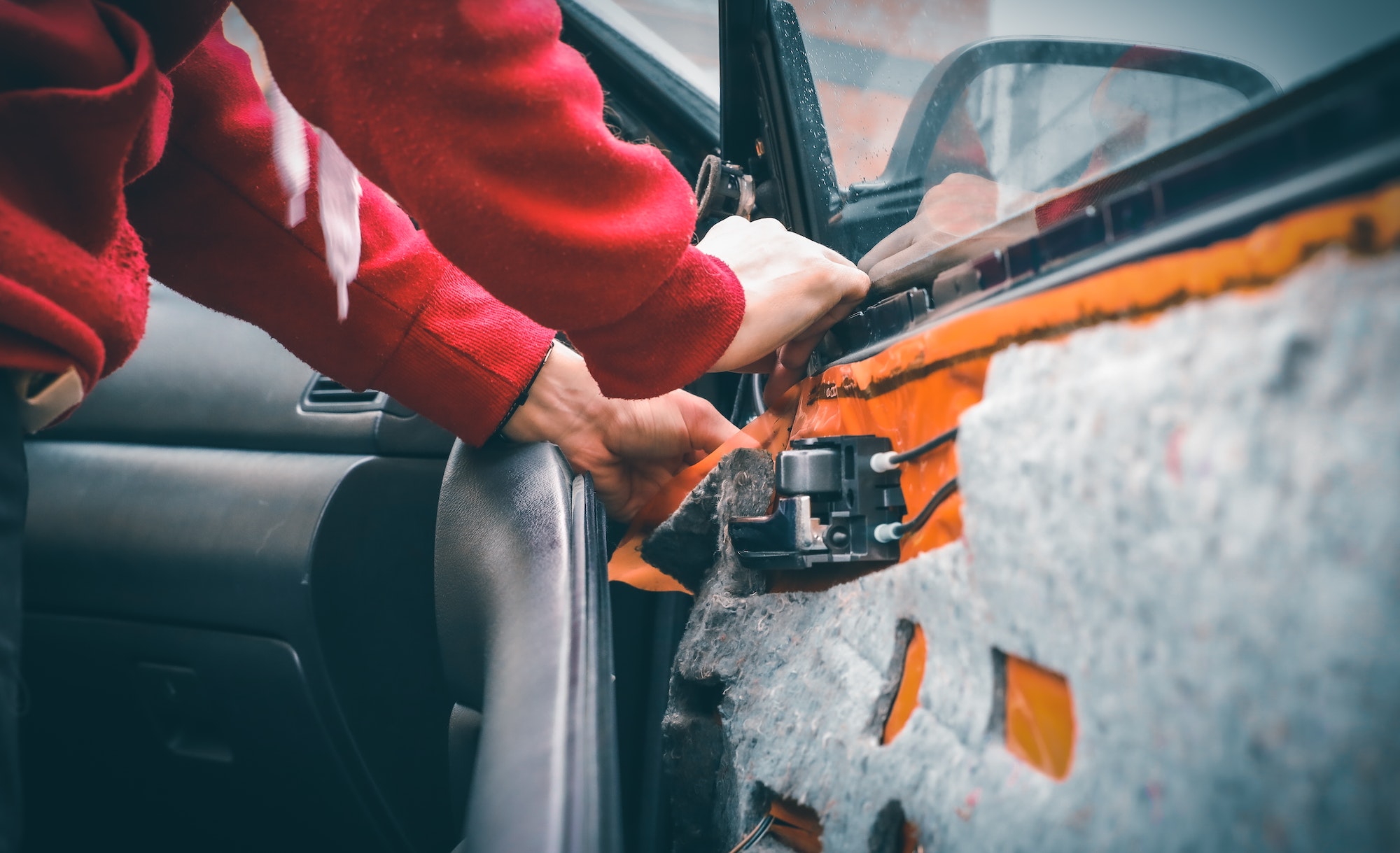A young Caucasian guy in a red body shirt repairs his car .