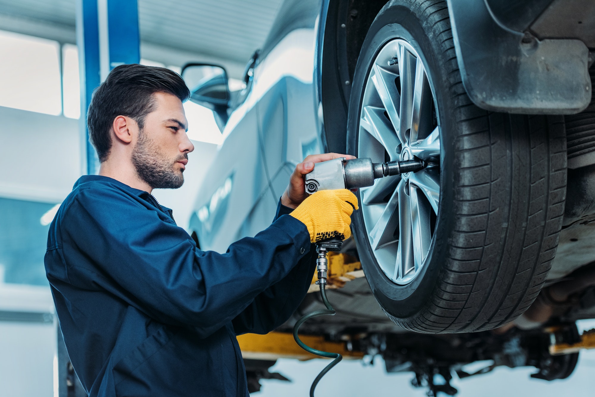 Automechanic unscrewing tire bolts on a lifted up car at a repair shop.