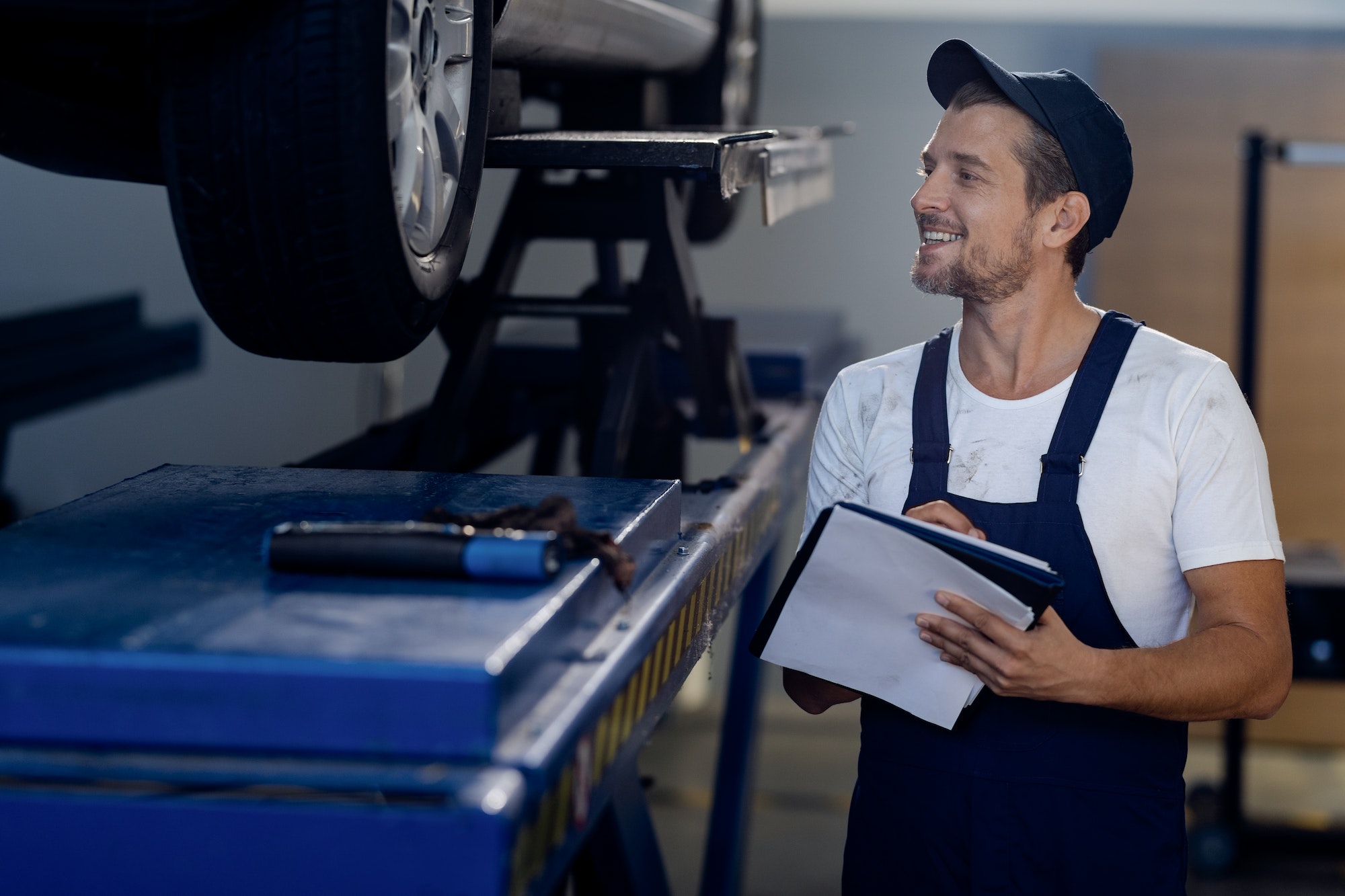 Happy mechanic taking notes while examining car in auto repair shop.